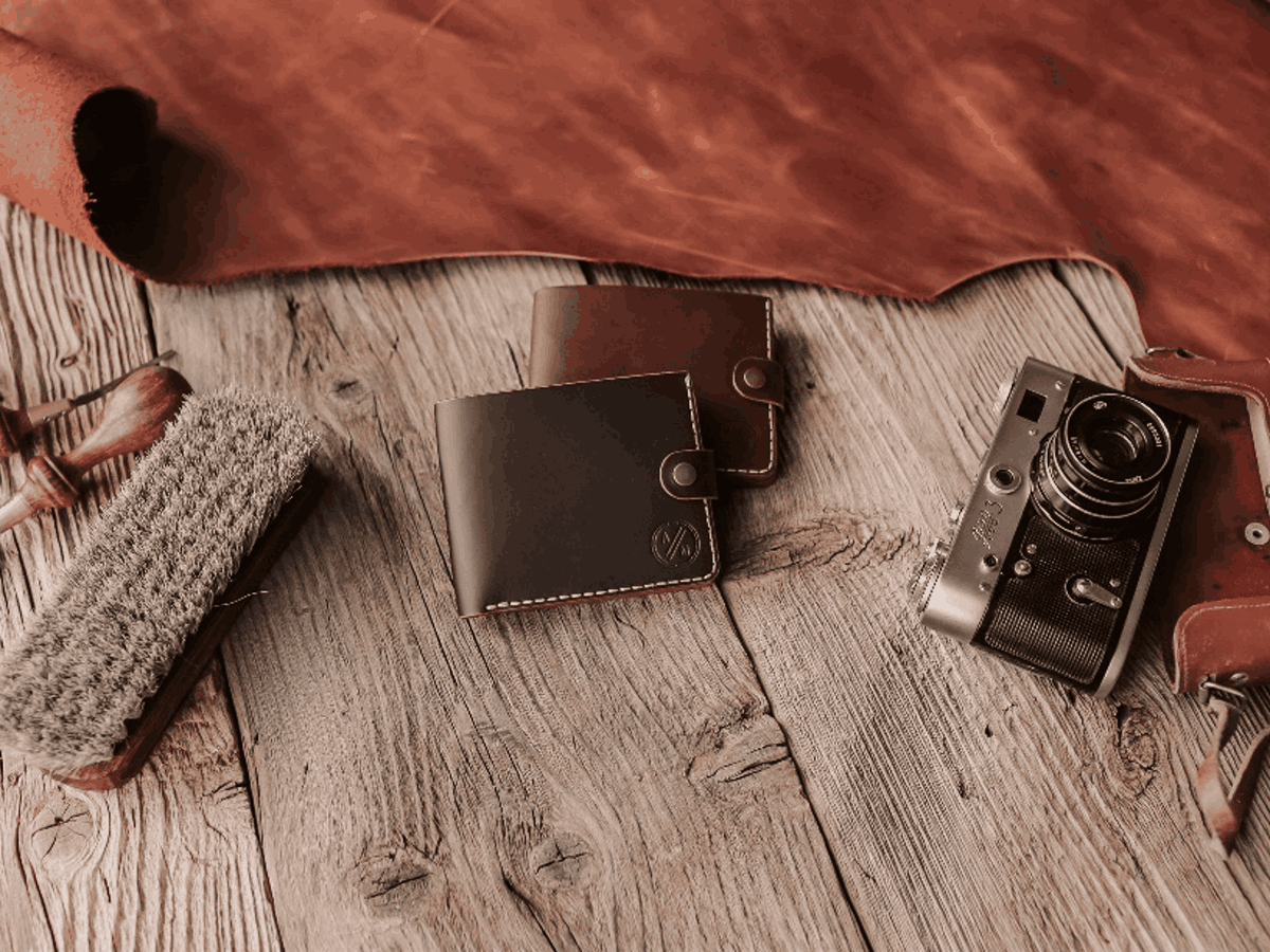 Two brown leather wallets and a camera on a wooden table, showing material and storage style for a Father's Day gift