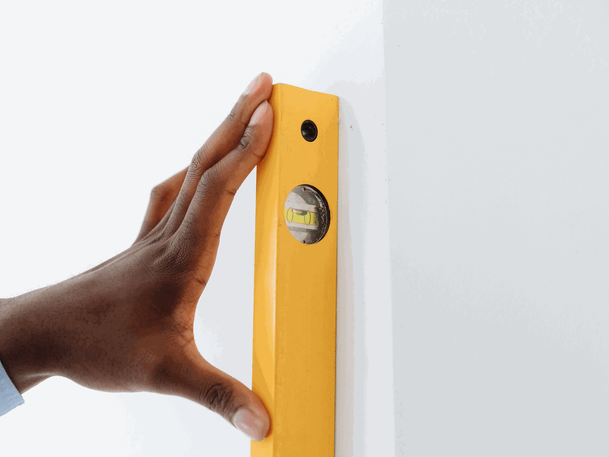 一隻手把黃色水平尺直立按在白色牆面上，水平尺中間的水泡停在刻度正中